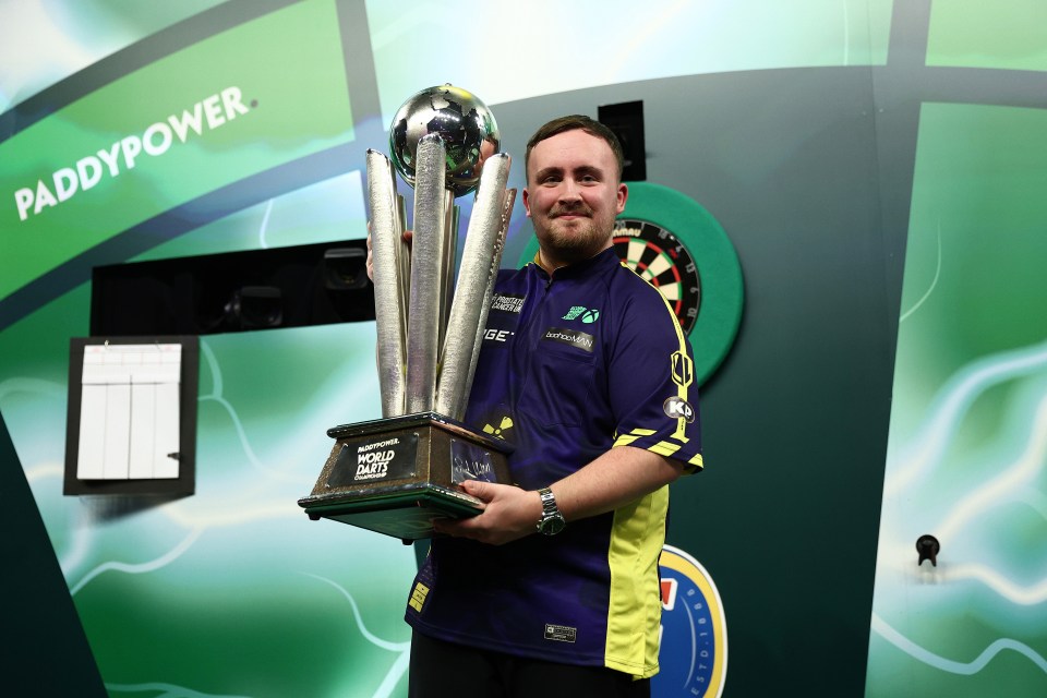 Luke Littler holding the Paddy Power World Darts Championship trophy.