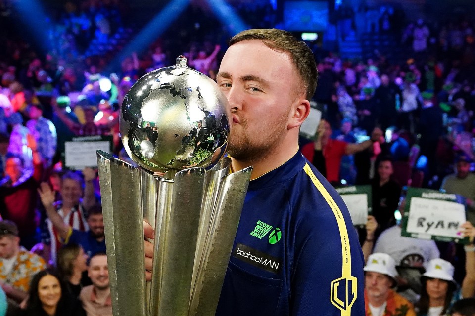 Luke Littler kissing the Sid Waddell Trophy after winning a darts championship.