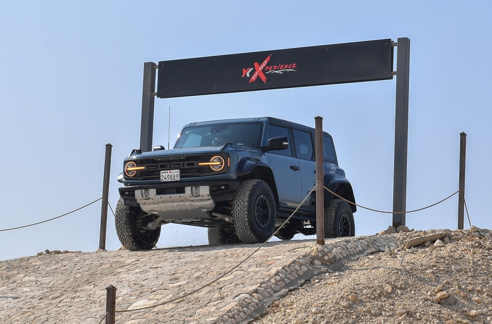 A blue Ford Bronco climbing a sand dune.