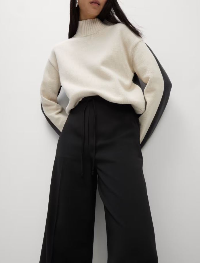 Woman wearing cream turtleneck sweater and black wide-leg trousers.