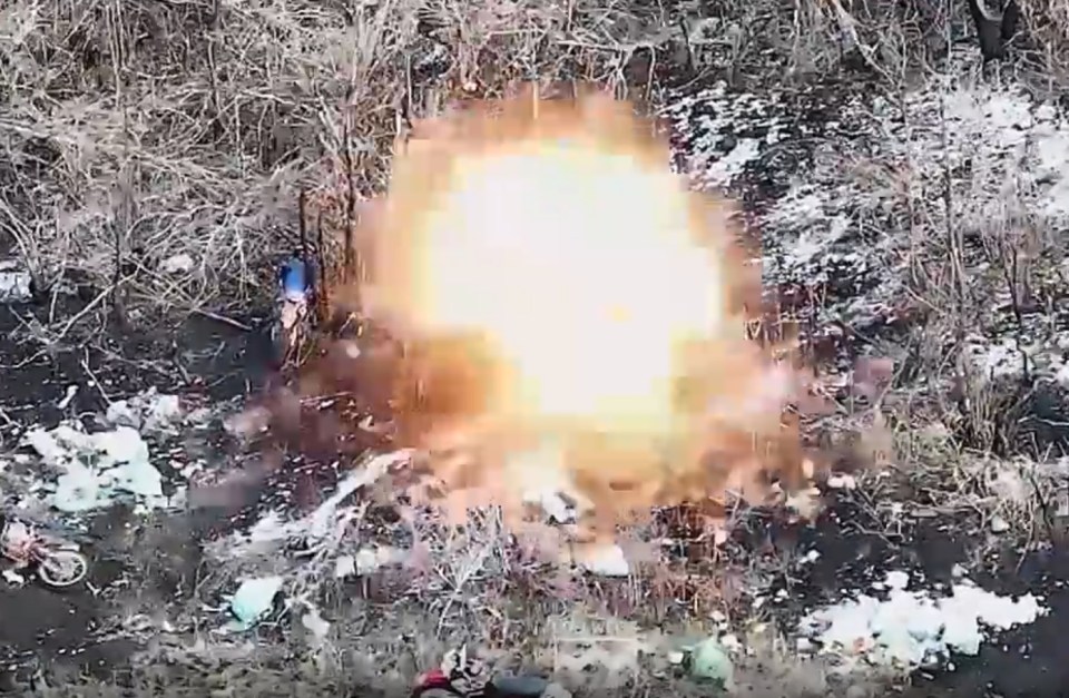 Drone footage of a large explosion near motorcycles in a wooded area.