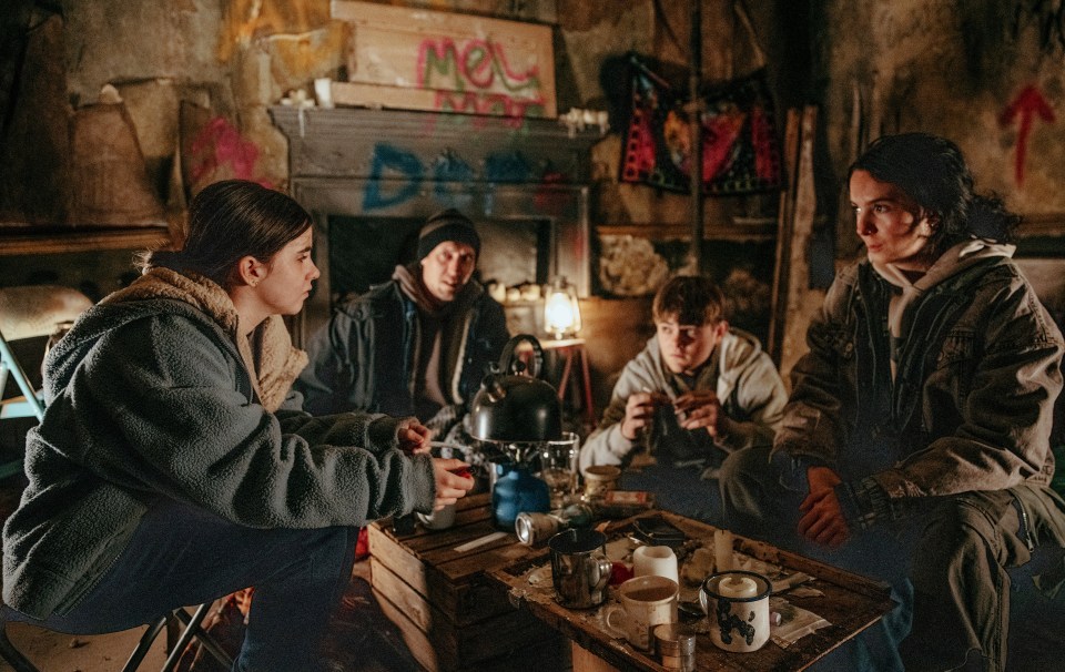 A still from Emmerdale showing April Windsor with three other characters in a dimly lit room.