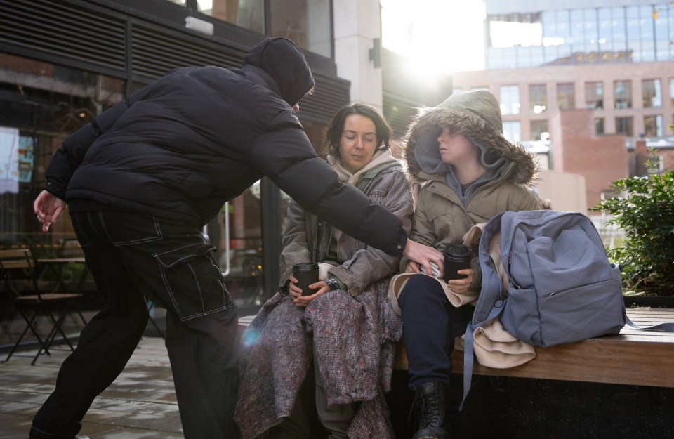 A person giving coffee to two people sitting on a bench.