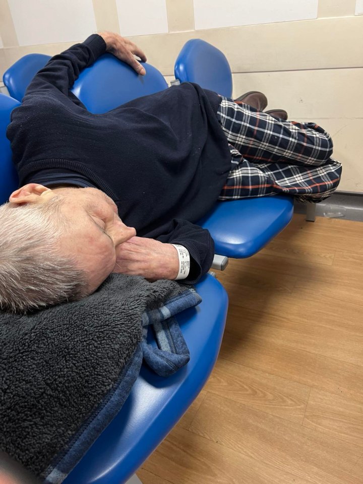 Elderly man sleeping on chairs in a hospital waiting room.