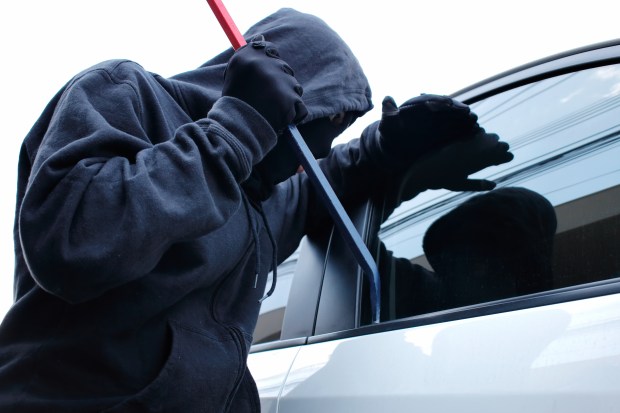 Masked burglar attempting to break into a car with a crowbar.