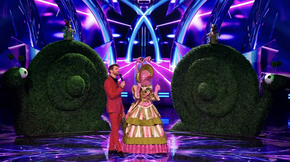 The Masked Singer Snail contestant on stage with a host.