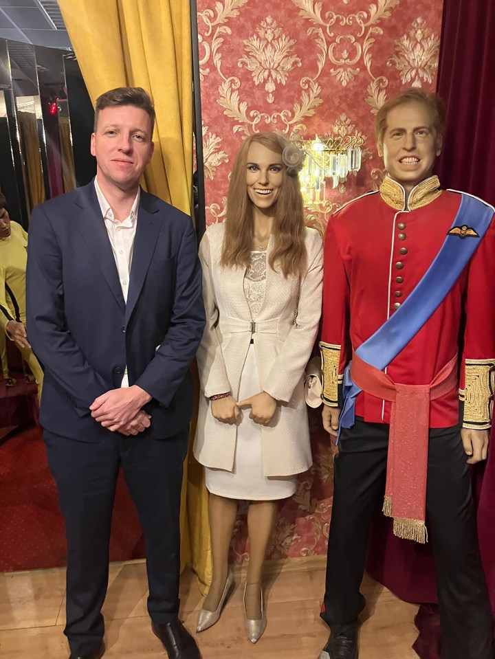 A man stands beside wax figures of Prince William and Kate Middleton.