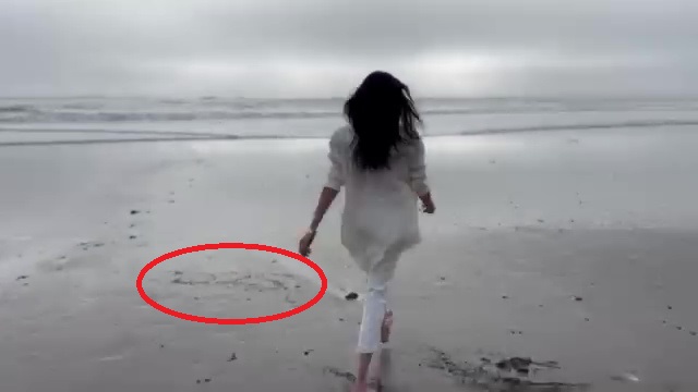 Meghan Markle walking on a beach with a message written in the sand.