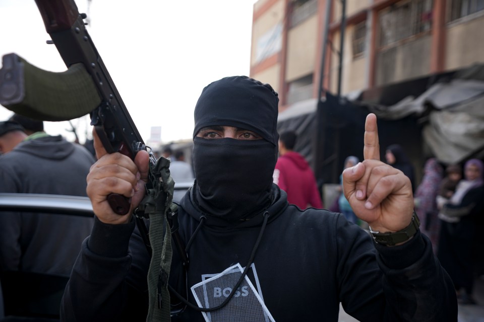 A masked member of the Izzedine al-Qassam Brigades holds a rifle and raises one finger.