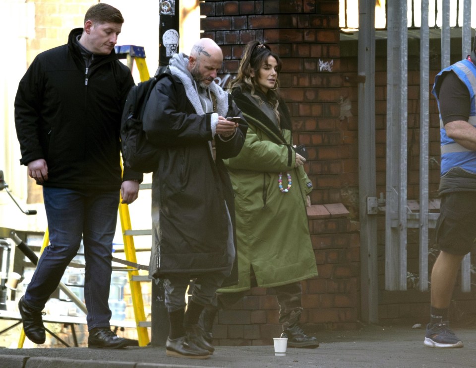 Michelle Keegan on a film set, accompanied by security.