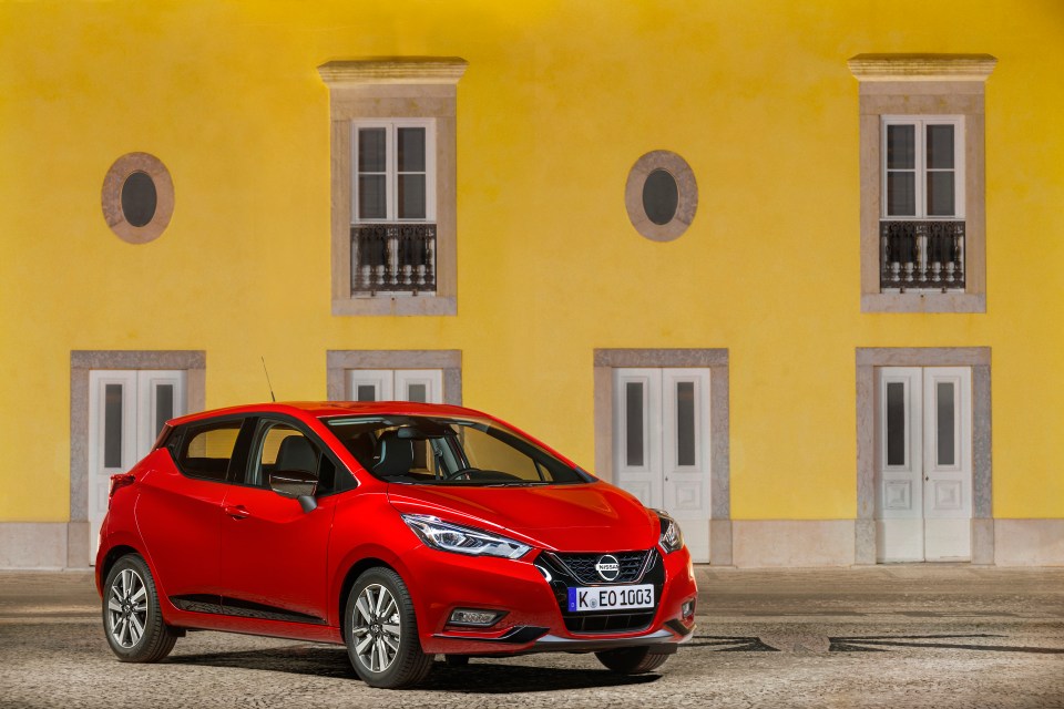 Red Nissan Micra parked in front of a yellow building.