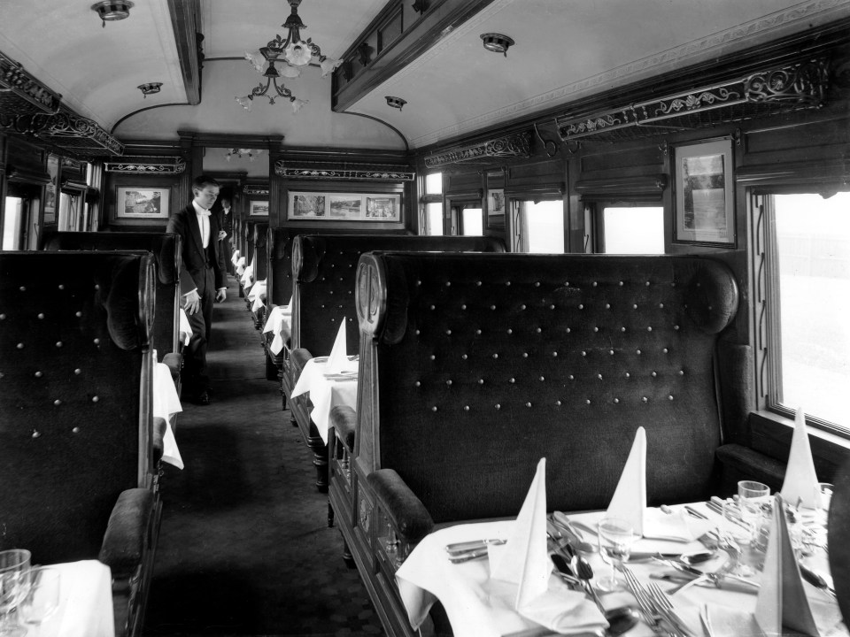 Interior of a vintage railway dining car with a waiter and set tables.