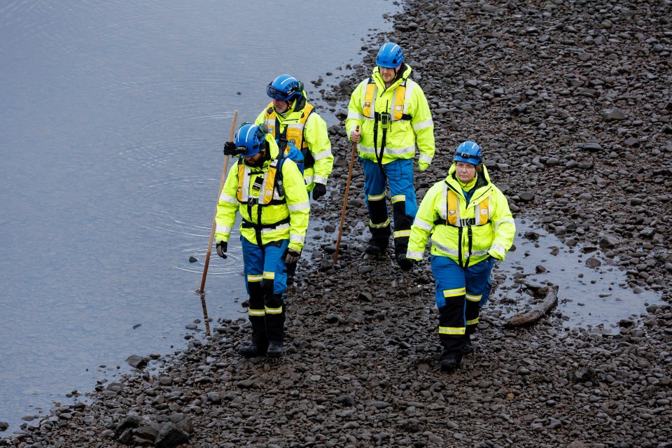 Coastguard officers searching a rocky riverbank.