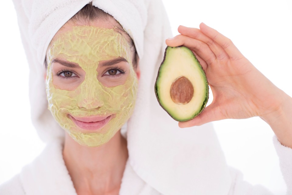 Woman with avocado face mask holding half an avocado.