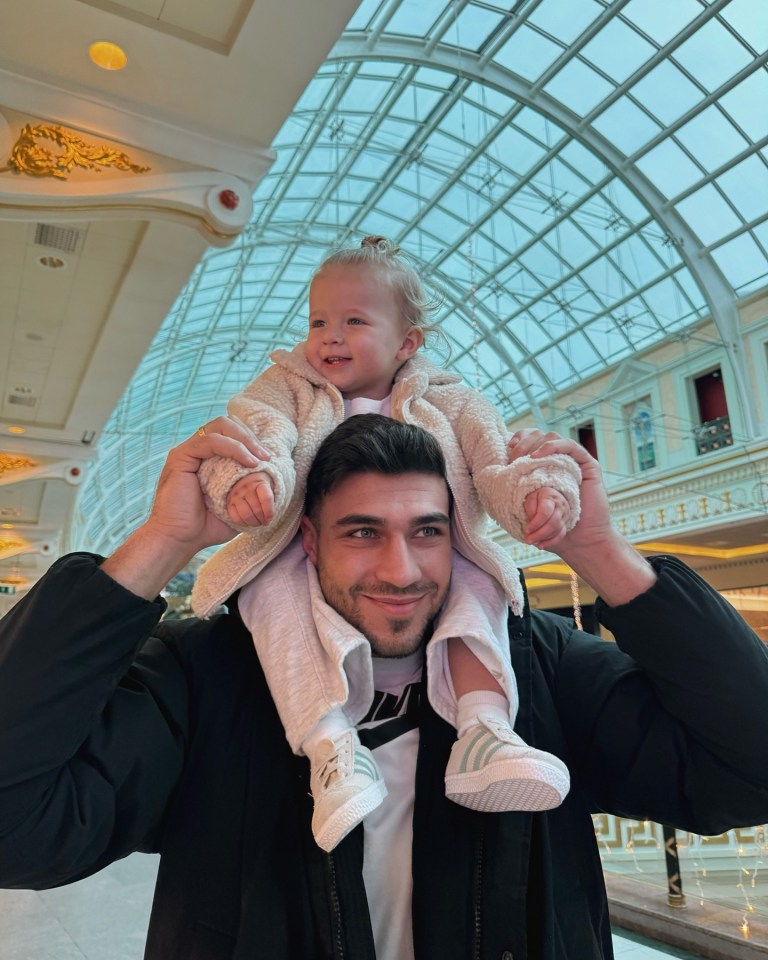 A man carries a toddler on his shoulders in a shopping mall.