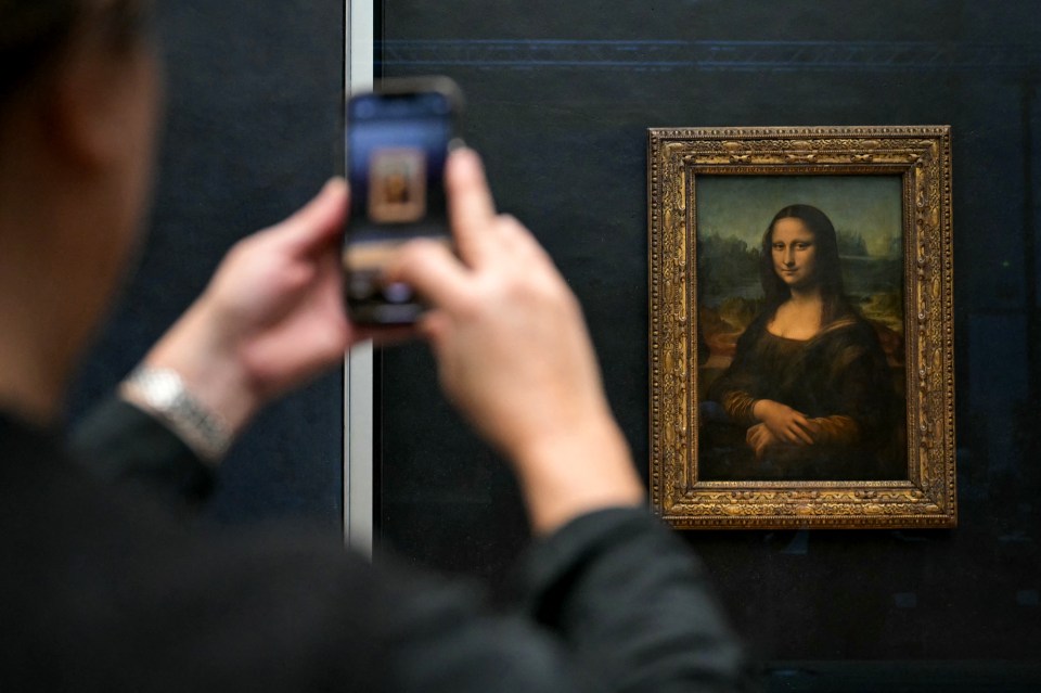 Person photographing the Mona Lisa at the Louvre Museum.