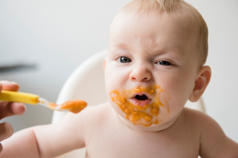 A messy baby being fed orange food puree.