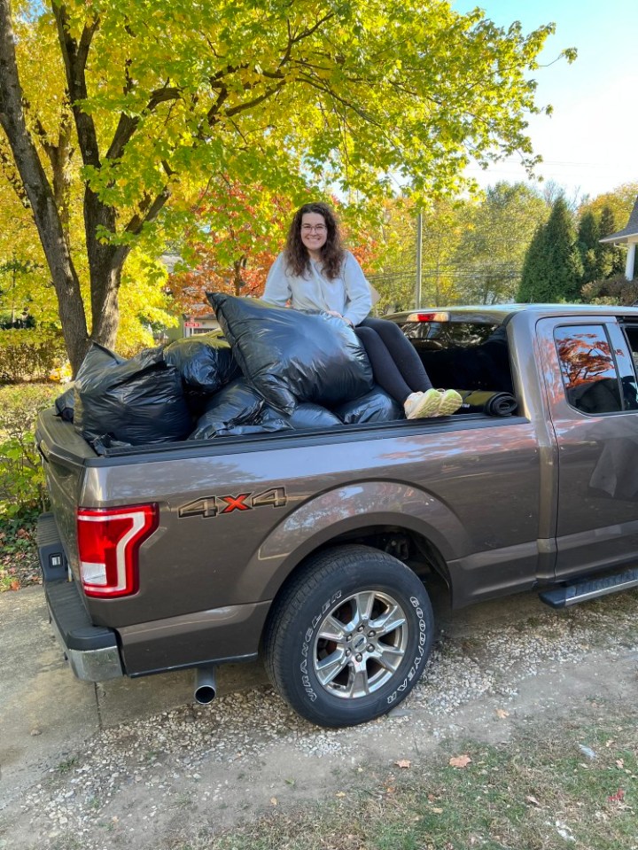 Woman sitting in truck bed filled with garbage bags.