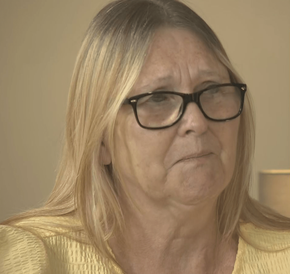 A woman with blonde hair and glasses speaks to the camera.