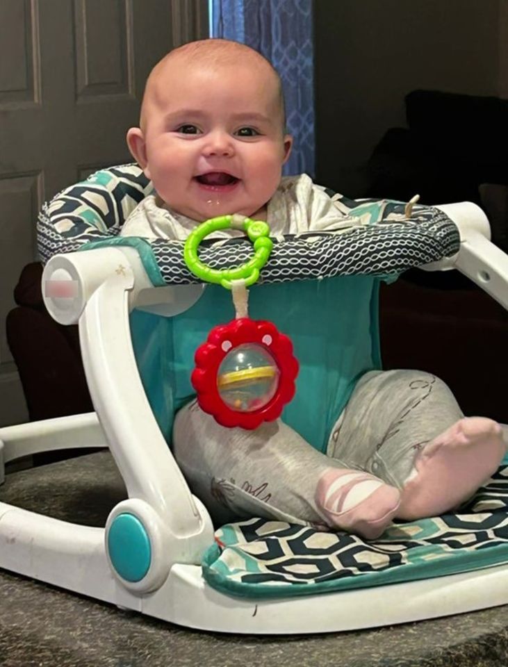 Smiling baby sitting in a teal and white baby seat.