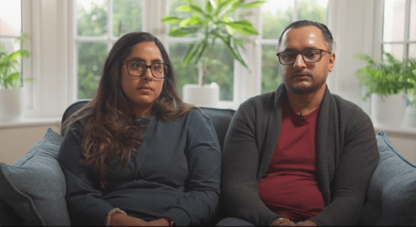 Couple sitting on a couch, looking at the camera.