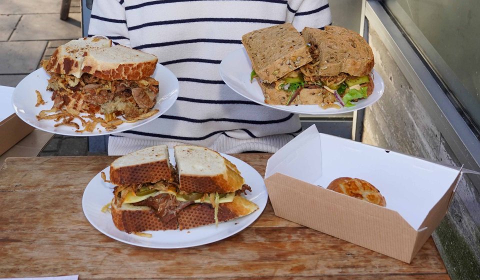 Person holding three large sandwiches and a bun.