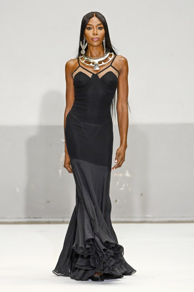 Naomi Campbell modeling a black gown at a fashion show.