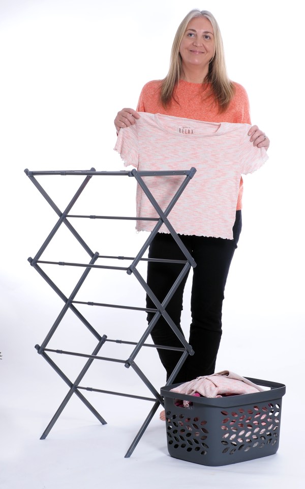 Woman holding a shirt near a clothes drying rack and laundry basket.