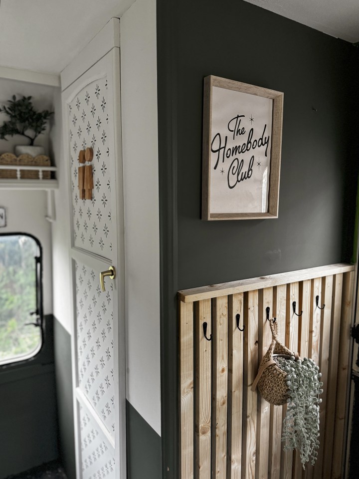 Renovated caravan interior with sage green walls and a "The Homebody Club" sign.