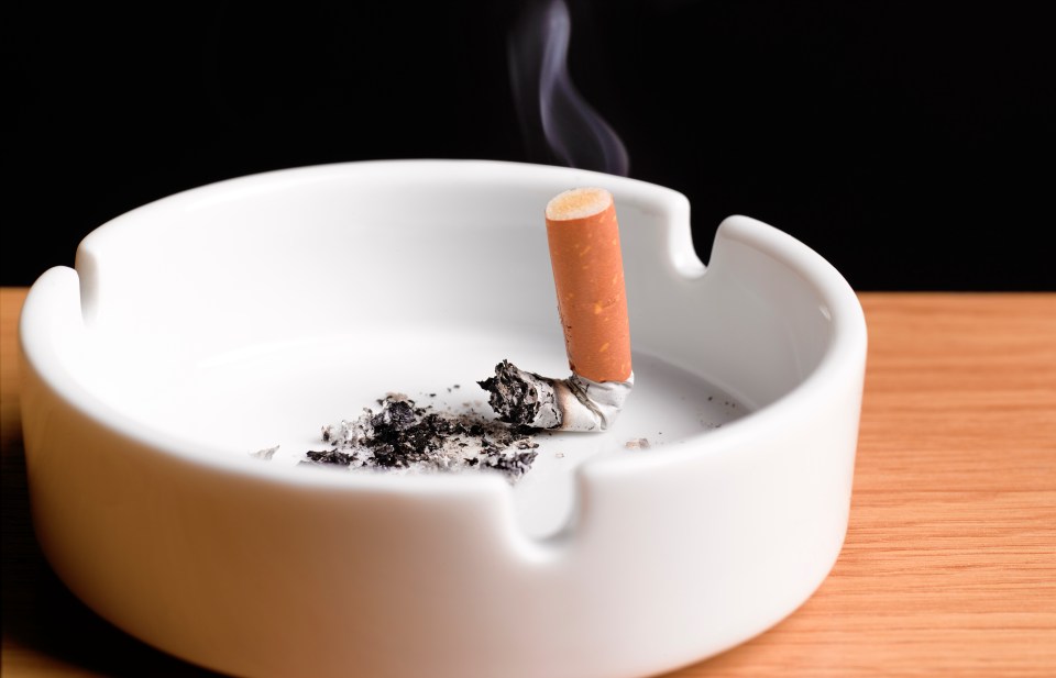 A partially smoked cigarette in a white ashtray.