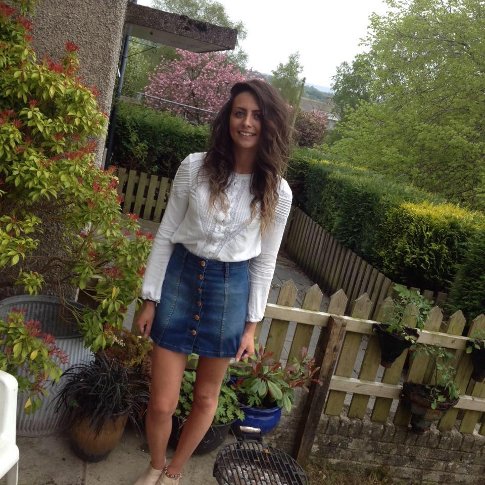 Photo of a young woman wearing a white blouse and denim skirt.