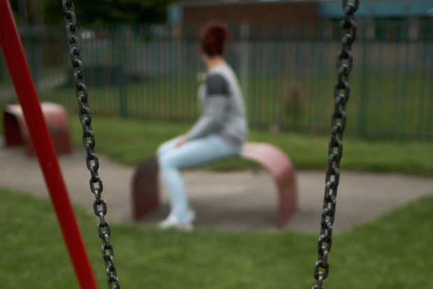 Swing chains in focus with a blurry person sitting on a bench in the background.