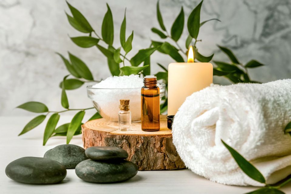 Spa treatment setup with essential oils, bath salts, candle, hot stones, and towel.