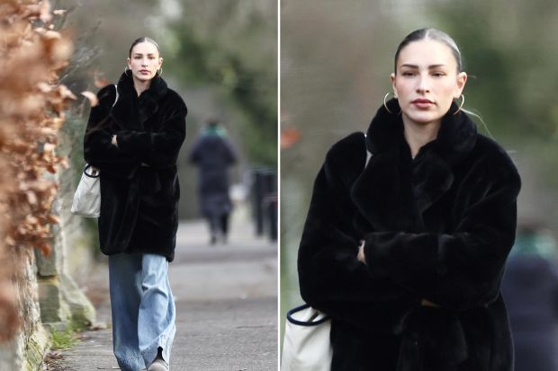 Woman in black coat and jeans walking down a path.