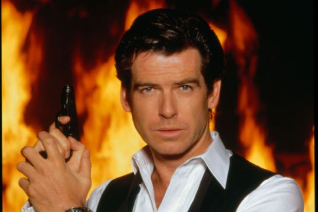 Pierce Brosnan holding a gun in front of a fiery background.