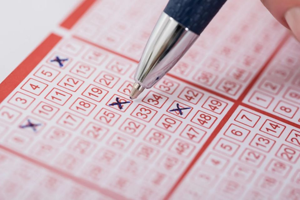 Close-up of a hand marking a lottery ticket with a pen.