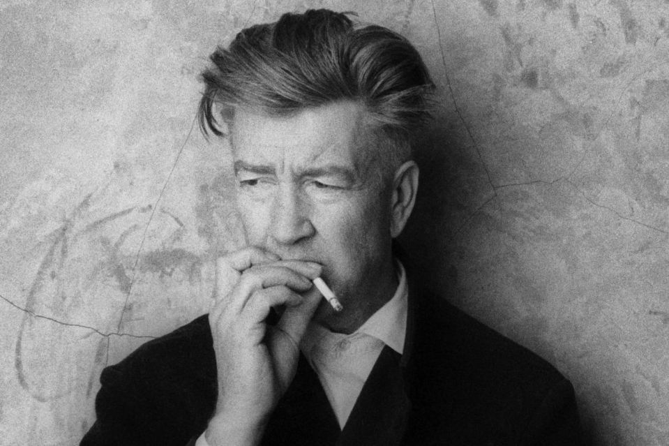 Black and white portrait of David Lynch smoking a cigarette.