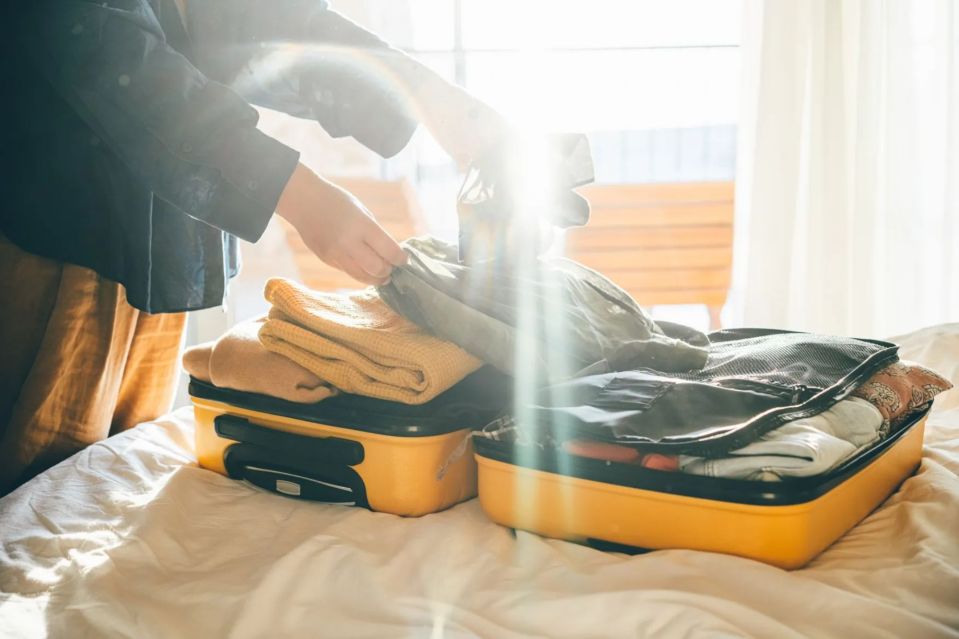 Person packing yellow suitcases on a bed.