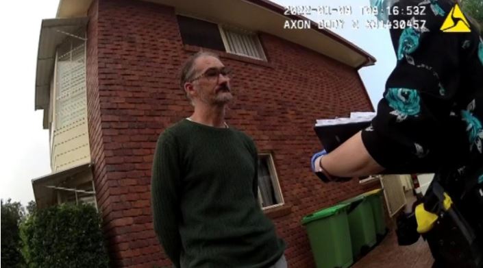 A man being interviewed by a police officer outside a brick building.