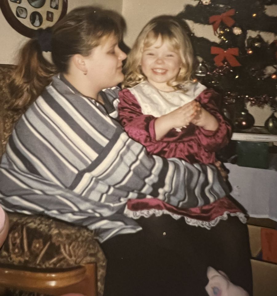 A mother and her young daughter sitting together in front of a Christmas tree.