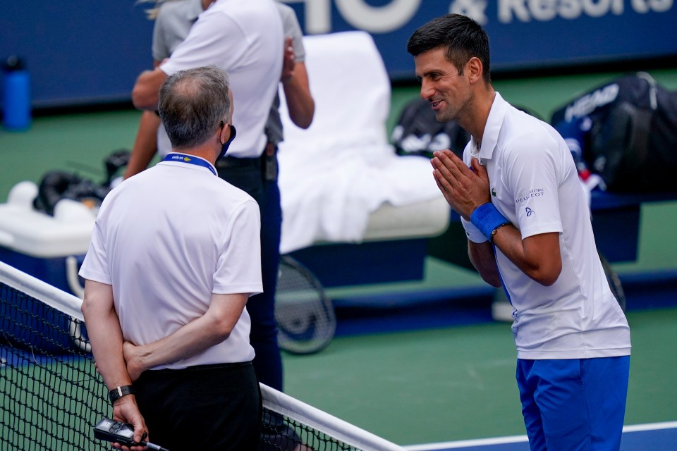 Novak Djokovic speaks with a tennis umpire after hitting a line judge with a ball.