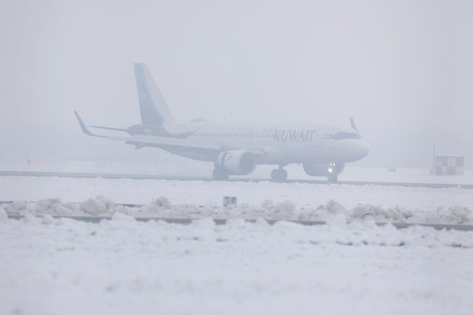 Kuwait Airways plane taxiing on a snow-covered runway in foggy conditions at Manchester Airport.