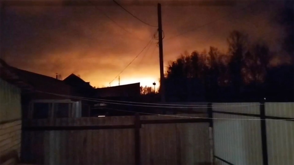 Orange glow of a large fire visible from behind a fence at night.