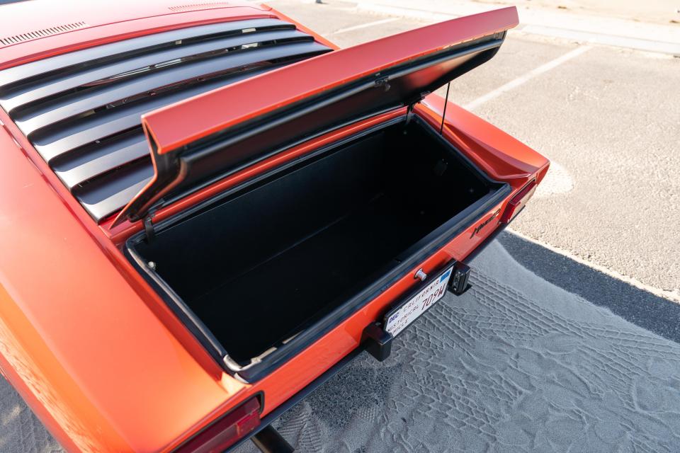 Rear view of an orange Lamborghini Miura P400 with its trunk open.