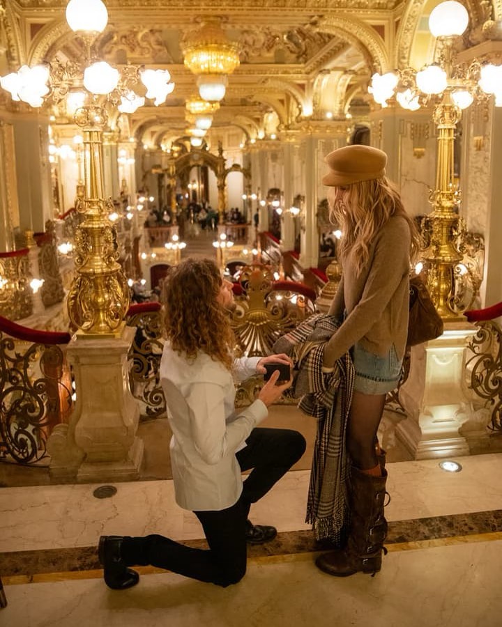 A man proposes to a woman in an ornate building.