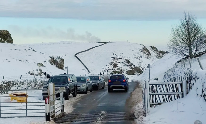 Cars parked on a snow-covered road, blocking access.