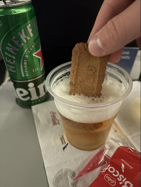 Biscoff biscuit being dipped into beer on an airplane.