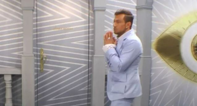 Paul Danan in a light blue suit, praying.