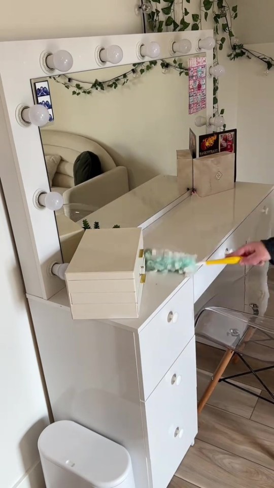 A person dusting a white vanity with a makeup mirror and lights.