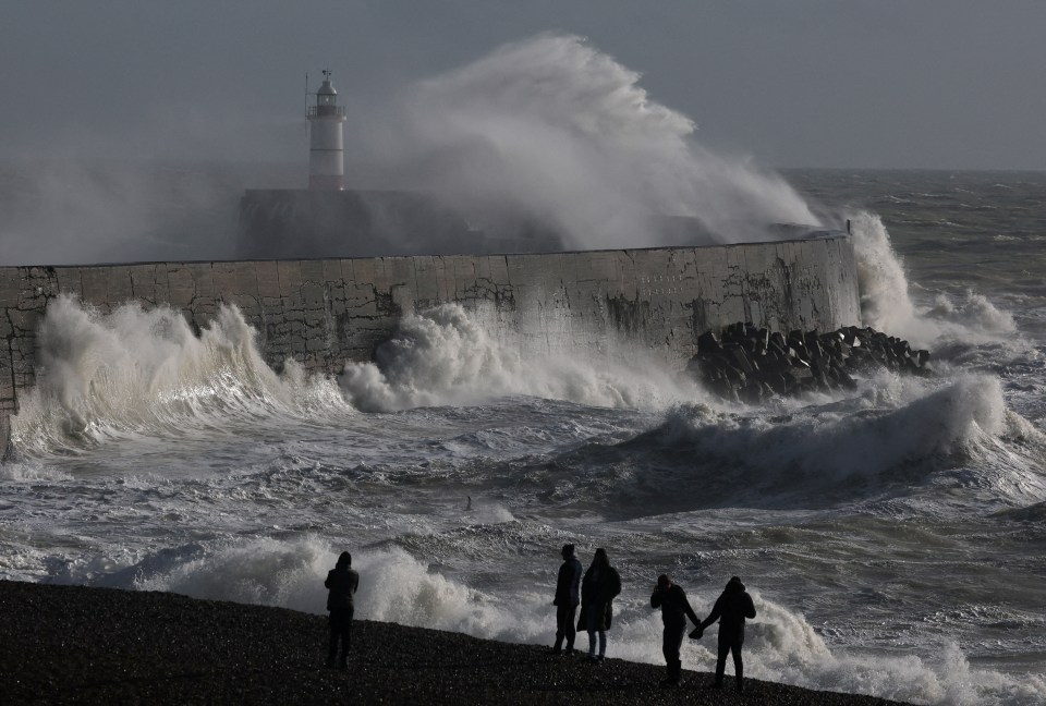 People watching large waves crash against a seawall during a storm.